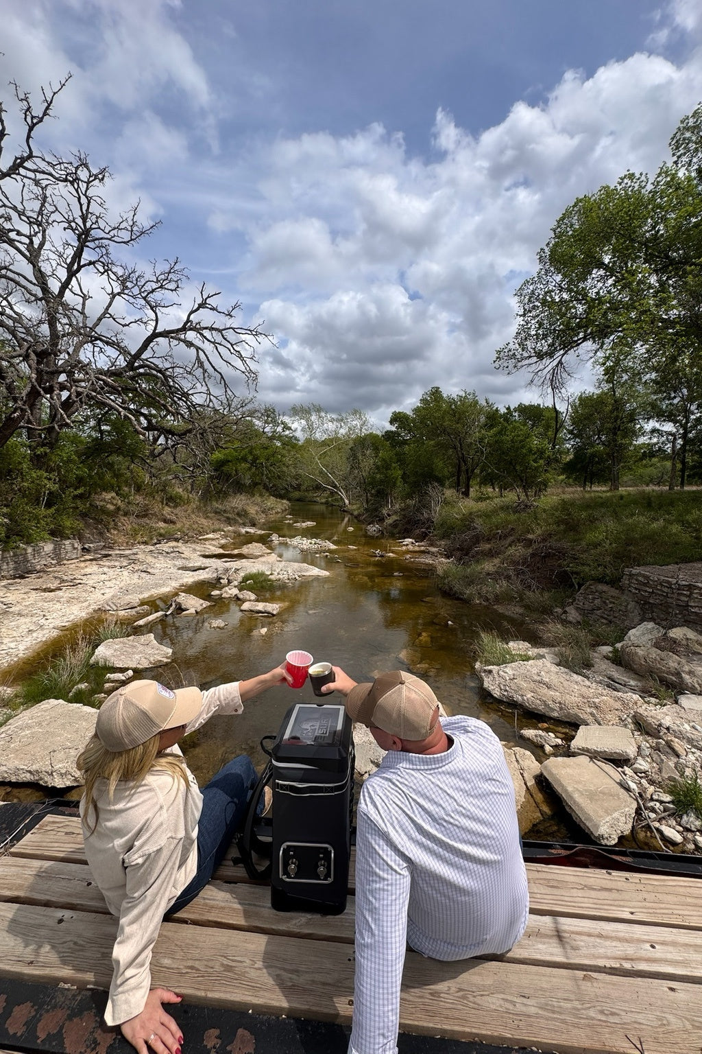 Two people raising SURV cups by a creek